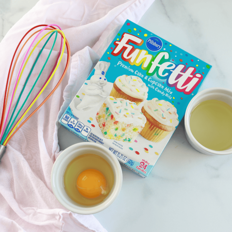 Ingredients for air fryer birthday cake including boxed cake mix, frosting, eggs, oil, and rainbow sprinkles
