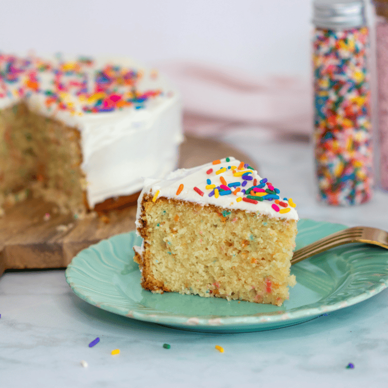 Air fryer birthday cake decorated with vanilla frosting, rainbow sprinkles, and lit birthday candles