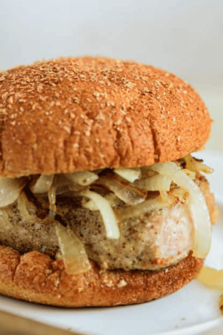Two air fryer pork chop sandwiches stacked, topped with sautéed onions on hamburger buns