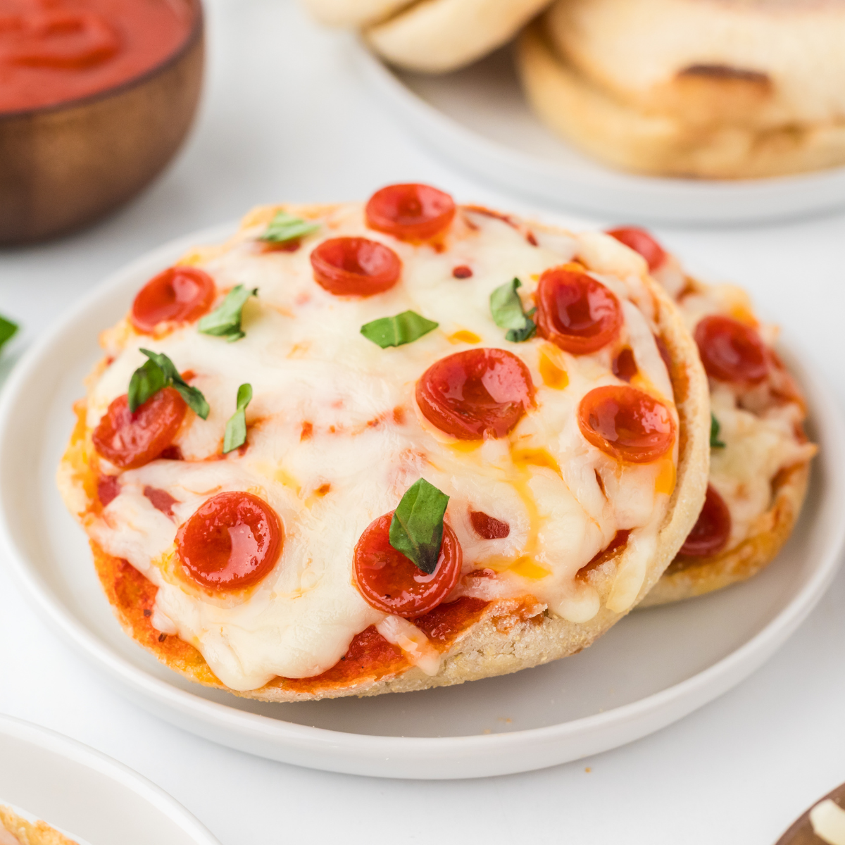 Four golden air fryer English muffin pizzas topped with melted mozzarella and mini pepperoni on a white plate