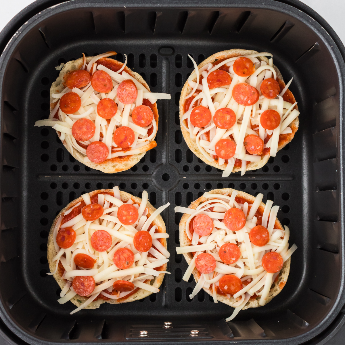 Assembled mini pizzas in the air fryer basket topped with sauce, mozzarella, and pepperoni ready to cook