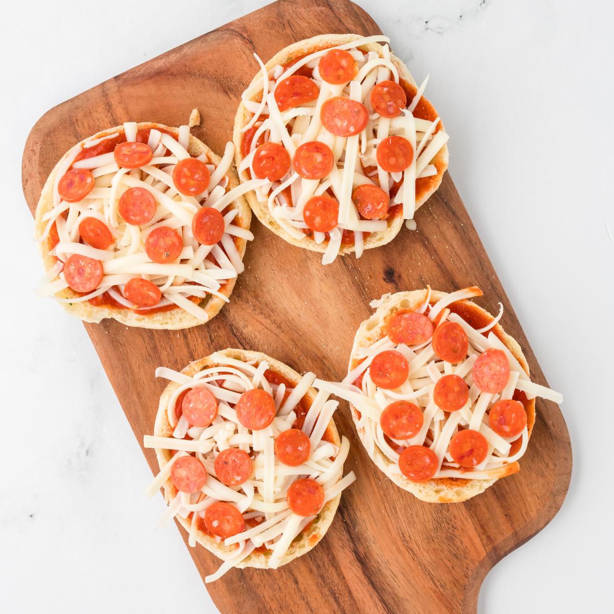 Split English muffins brushed with olive oil arranged cut-side up in the air fryer basket for pre-toasting