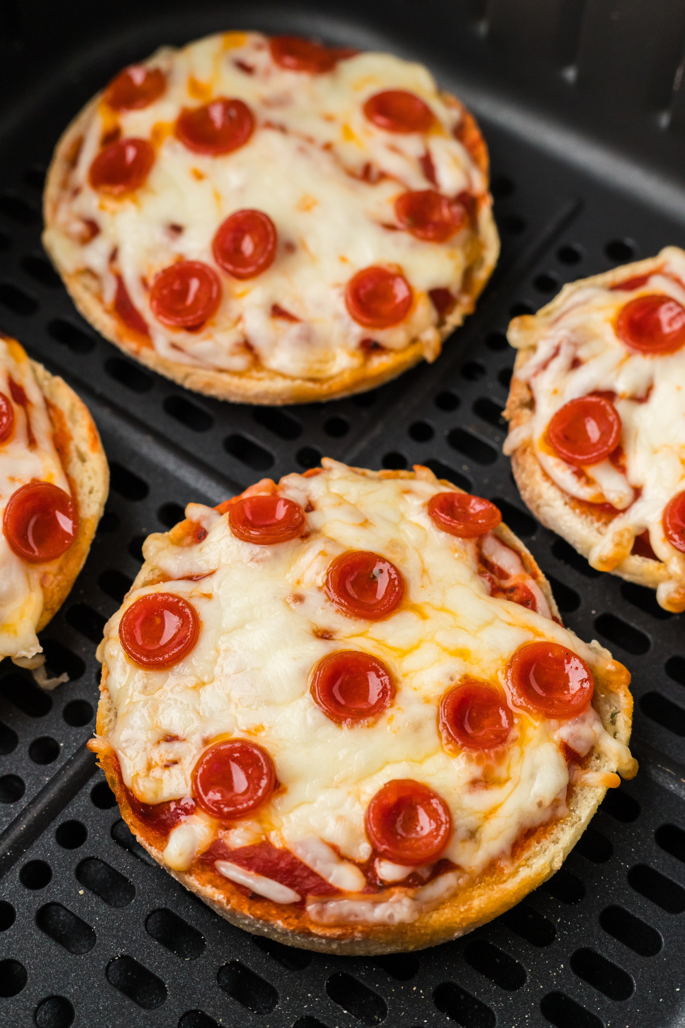 Stack of finished air fryer English muffin pizzas with melted cheese stretching between them