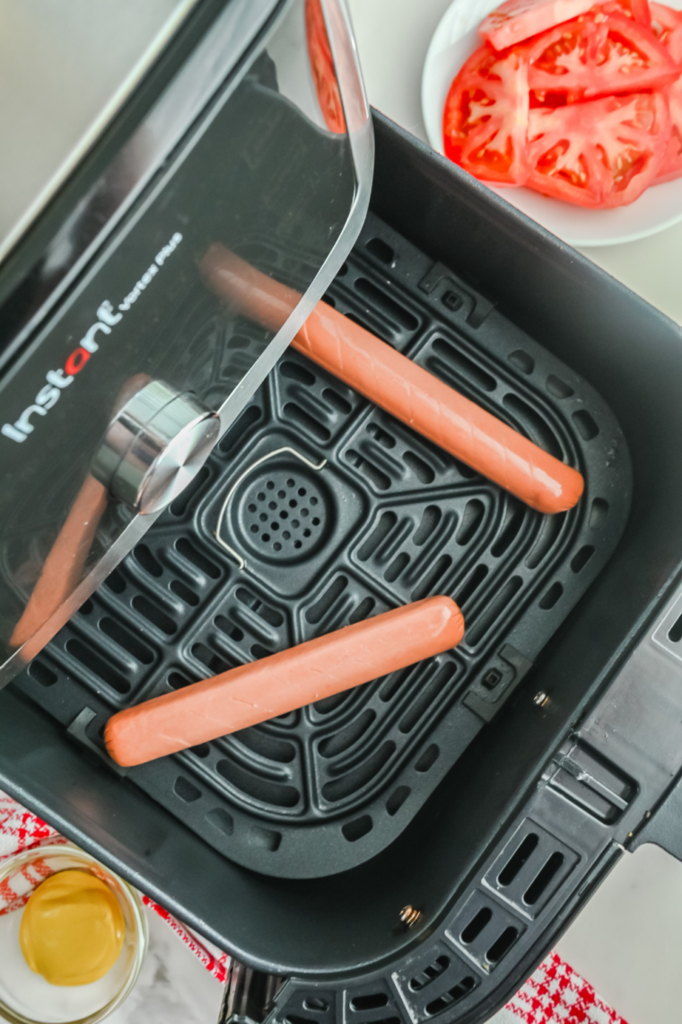 Hot dogs placed in a single layer in air fryer basket with space between.