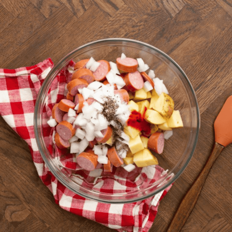 Sliced kielbasa and diced potatoes in a large bowl ready for seasoning and cooking.