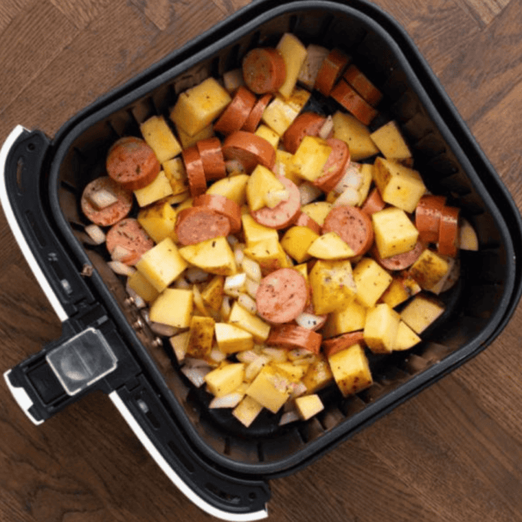Seasoned kielbasa and potatoes spread evenly in air fryer basket ready to cook at 370°F.