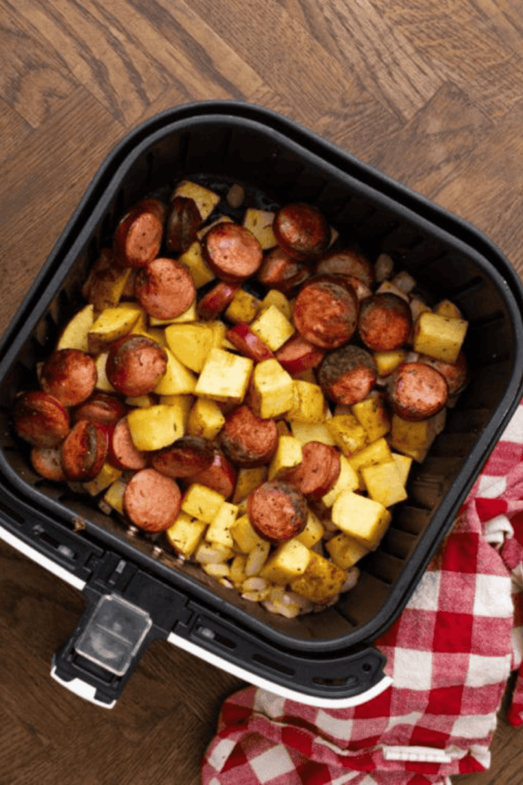 Golden, crispy air fryer kielbasa and potatoes cooked and resting in the air fryer basket.