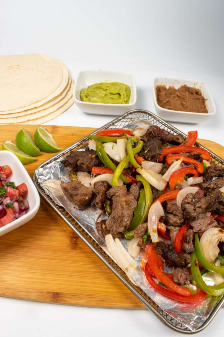 Two air fryer steak tacos on a plate with juicy ribeye slices, fresh toppings, and lime wedges