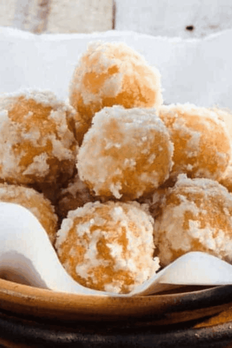A mountain of golden-brown air fryer zeppole dusted with a thick layer of powdered sugar on a serving plate.