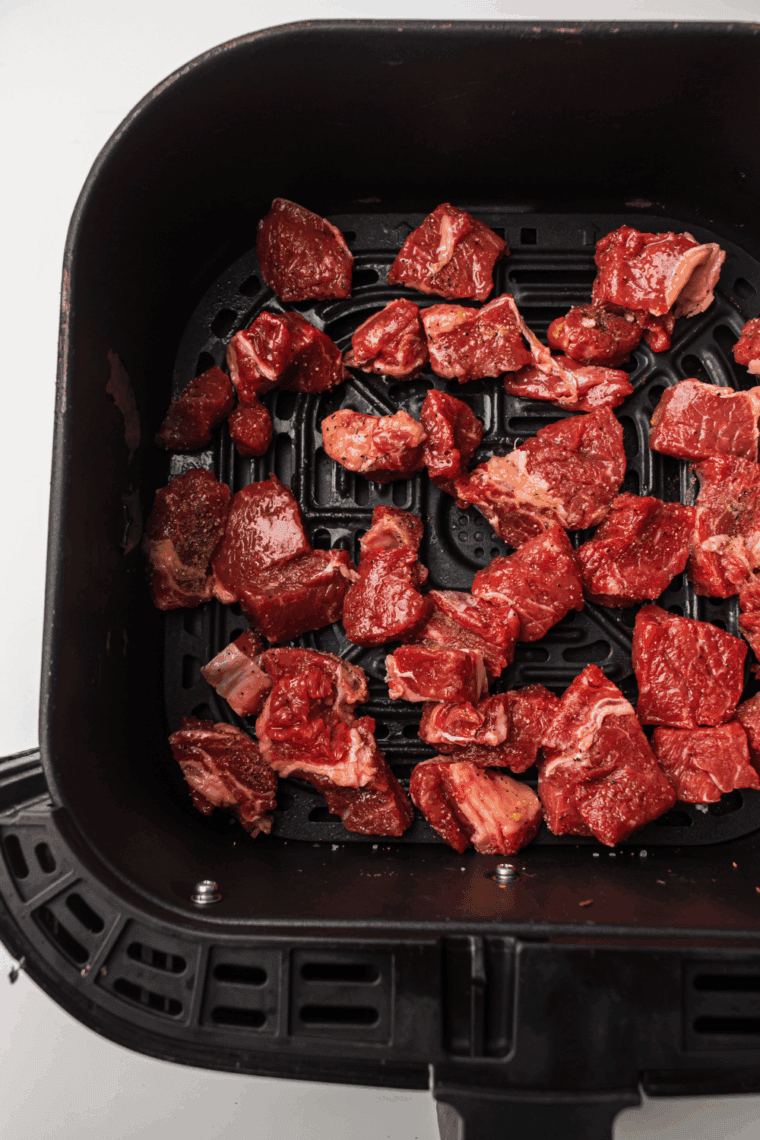 Marinated steak tips cooking in air fryer basket, flipping halfway through