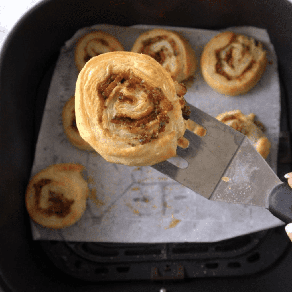 Golden brown air fryer breakfast pinwheels filled with scrambled eggs, melted cheese, and bacon, served on a white plate