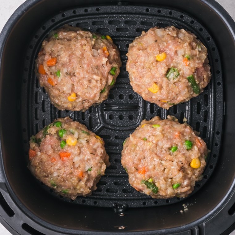 Raw chicken patties arranged in a single layer in a parchment lined air fryer basket