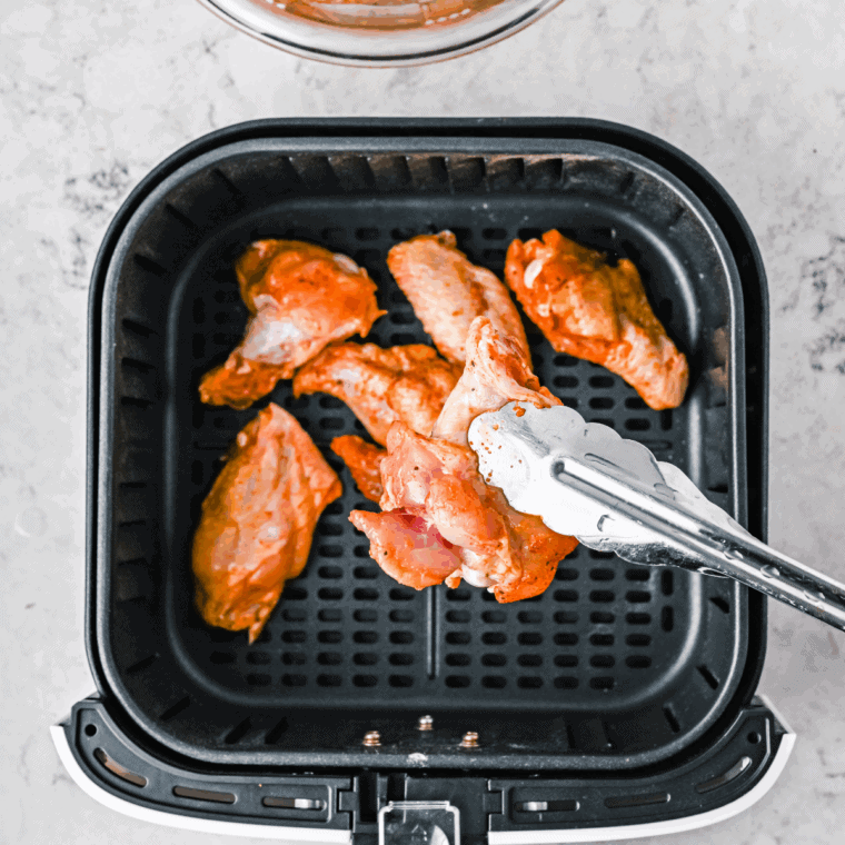 Placing seasoned chicken wings in the air fryer basket, spraying with vegetable oil, and air frying until golden and crispy.