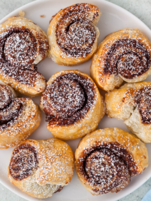 Golden air fryer Nutella puff pastry bites stacked on a white plate and dusted with powdered sugar