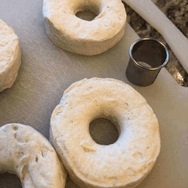 Cutting holes in canned biscuit dough to shape donuts and donut holes on a cutting board