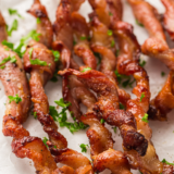 Crispy strips of Ninja Crispi bacon resting on the crisper plate inside the glass container, PowerPod lifted above