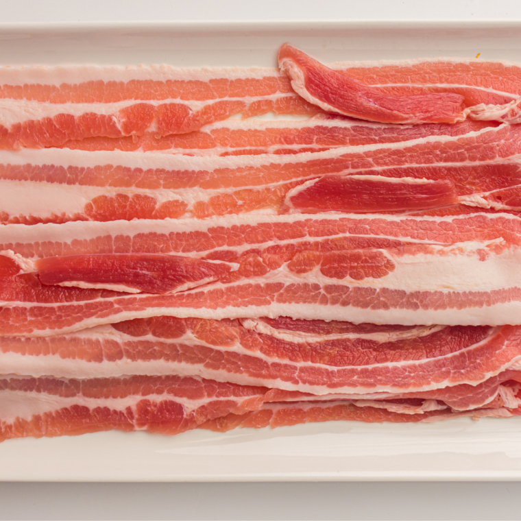 Six raw bacon strips fanned out on parchment beside the Ninja Crispi glass container and crisper plate