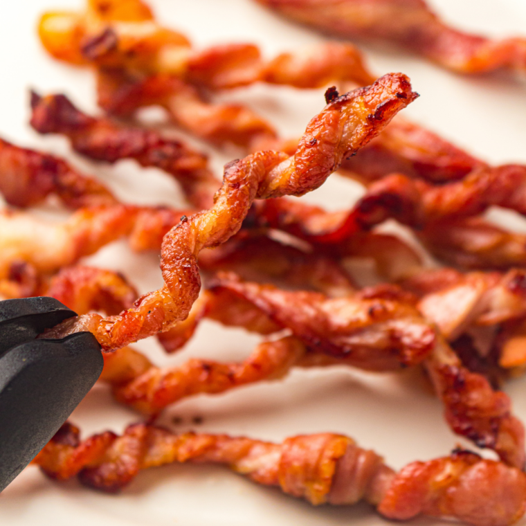 Cooked bacon draining on a paper-towel-lined plate beside the open Ninja Crispi container
