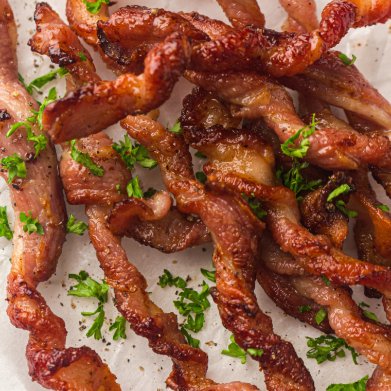Golden bacon strips mid-cook in the Ninja Crispi glass air fryer, fat pooled below the crisper plate