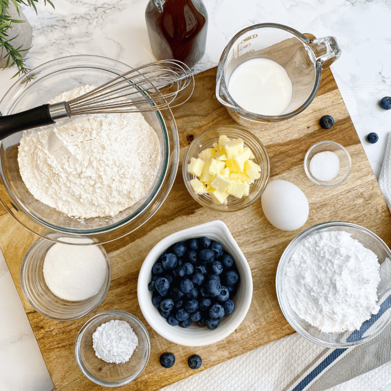 Ingredients for air fryer blueberry scones — flour, sugar, butter, eggs, cream, and fresh blueberries — on a kitchen table