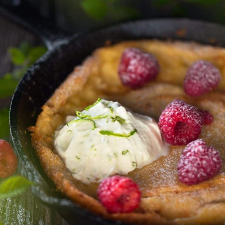 Finished Dutch baby with powdered sugar, lemon wedge, and fresh raspberries.