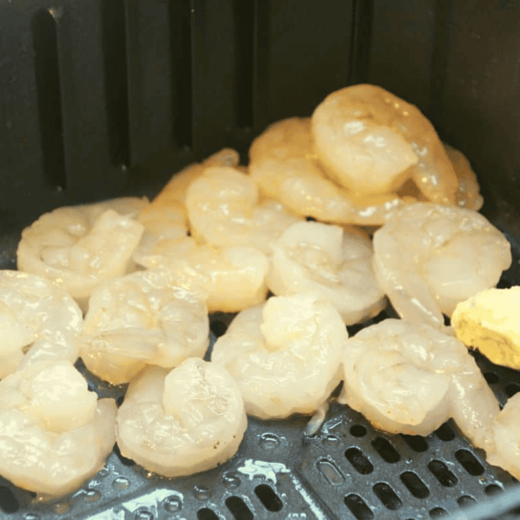 Shrimp arranged in an air fryer basket ready to cook at 400°F, midway through flipping.