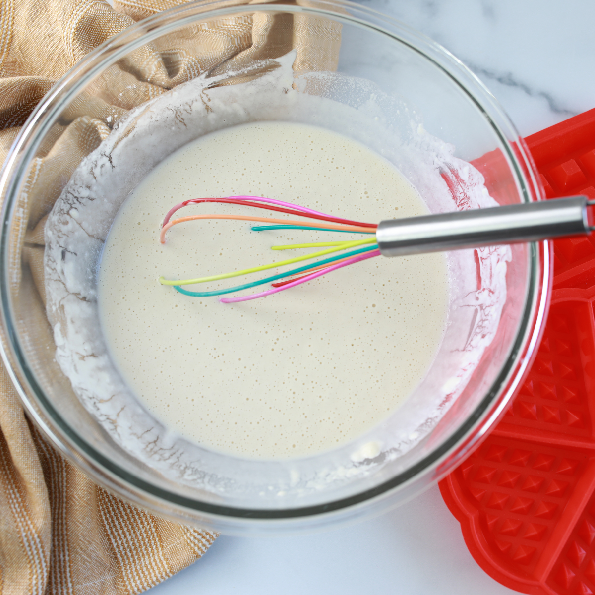 Smooth waffle mix in glass bowl, with whisk.
