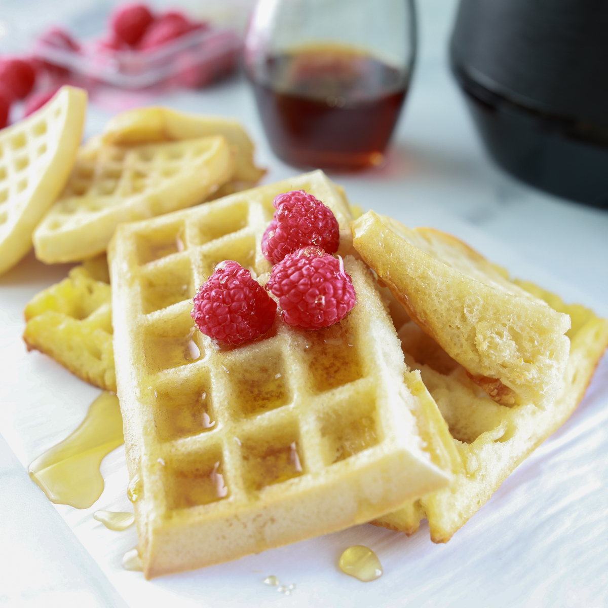 Golden homemade waffles made in the air fryer, topped with butter and maple syrup on a white plate.