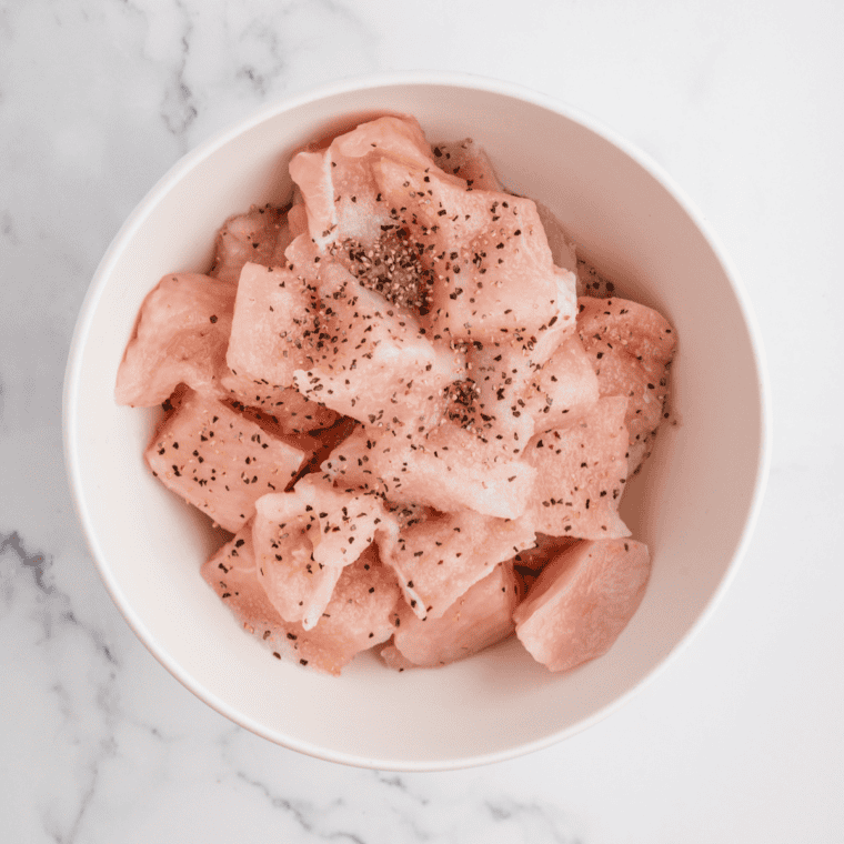 Raw chicken pieces being seasoned with salt and pepper next to a bowl of flour and baking powder.