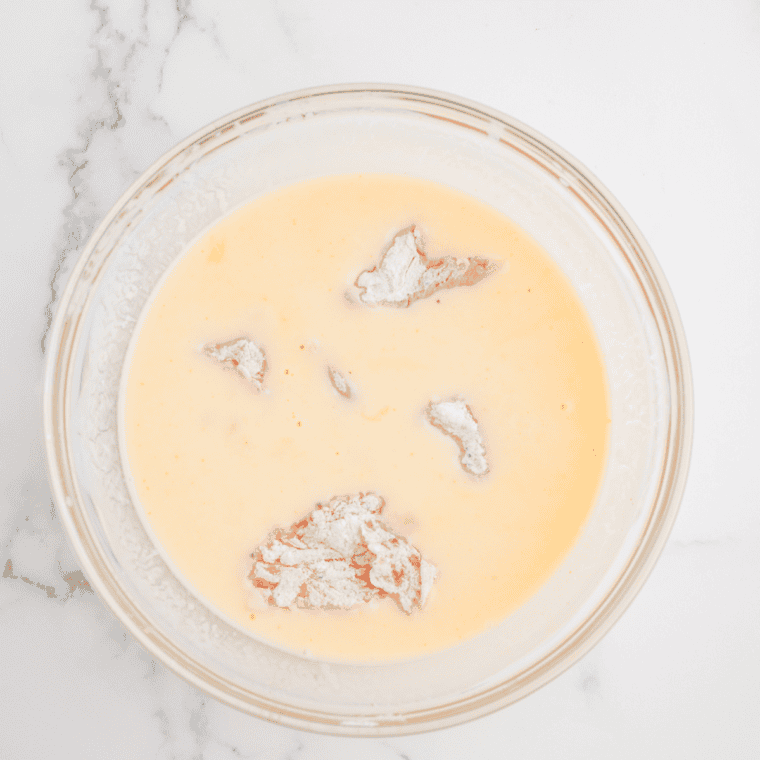 Chicken pieces being double-dipped—first in buttermilk mixture, then back into the seasoned flour for a crispy coating.