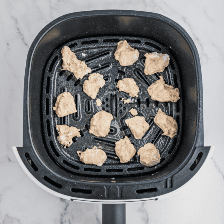 Coated chicken pieces arranged in an air fryer basket sprayed with olive oil, ready for cooking without overcrowding.
