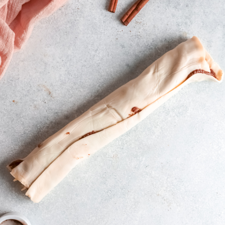 Spreading pumpkin spice mixture on puff pastry and rolling into a log before slicing into cinnamon rolls.