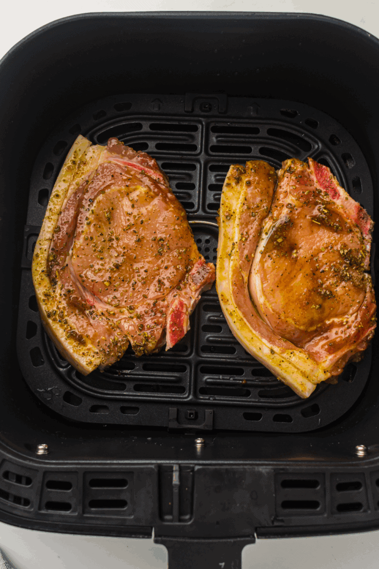Pork chops in the air fryer basket, flipping halfway, cooking until 145°F internal temperature.