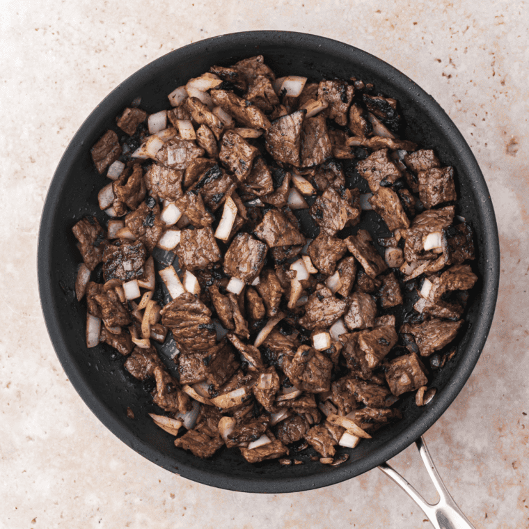 Skillet cooking with olive oil, sautéed onions, and chopped steak until browned.
