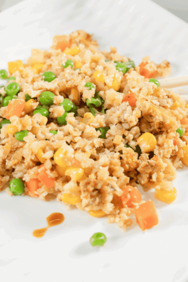 Benihana-style garlic chicken cauliflower fried rice served on a plate with colorful vegetables and green onions.