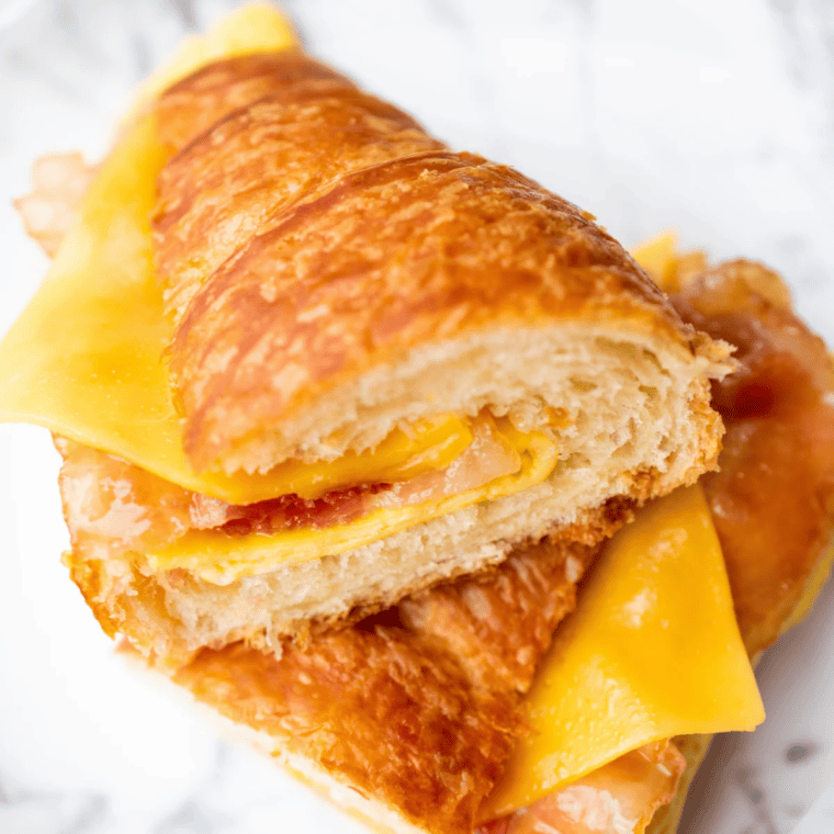 Two air fryer breakfast croissant sandwiches with candied bacon, fried eggs, and melted cheese on a plate.