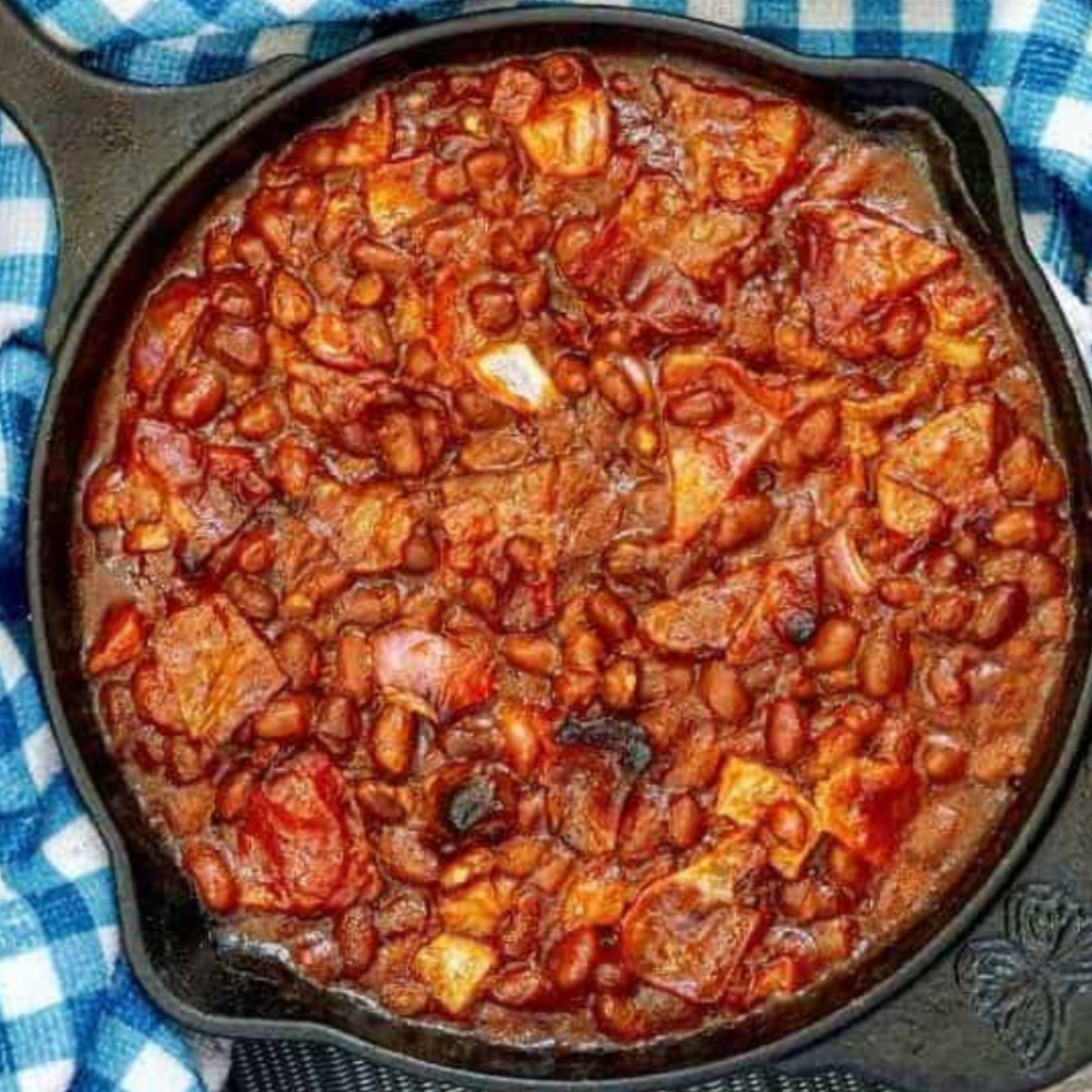Cooked baked beans bubbling in a cast iron skillet, showcasing a rich, savory sauce and topped with crispy bacon bits.