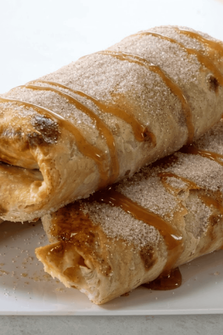 Golden air fryer apple pie taquitos dusted with cinnamon sugar on a white plate
