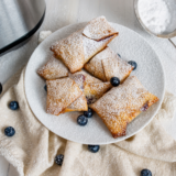 Air fryer blueberry egg rolls dusted with powdered sugar on a white plate