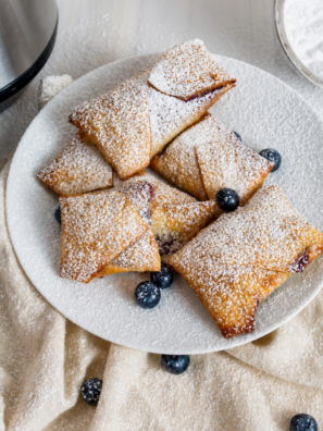 Air fryer blueberry egg rolls dusted with powdered sugar on a white plate