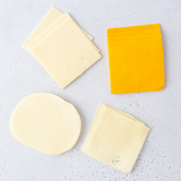 Ultra thin cheddar cheese slices being cut into four squares on a cutting board