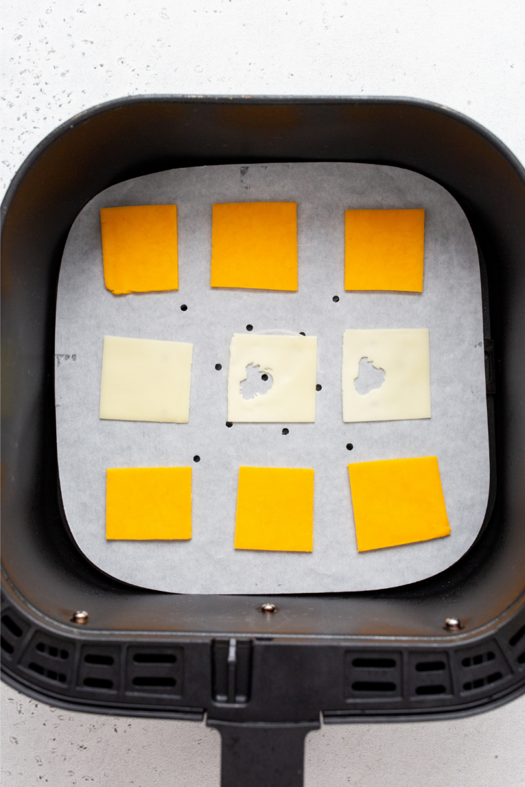 Cheese squares spaced in a single layer on parchment in an air fryer basket