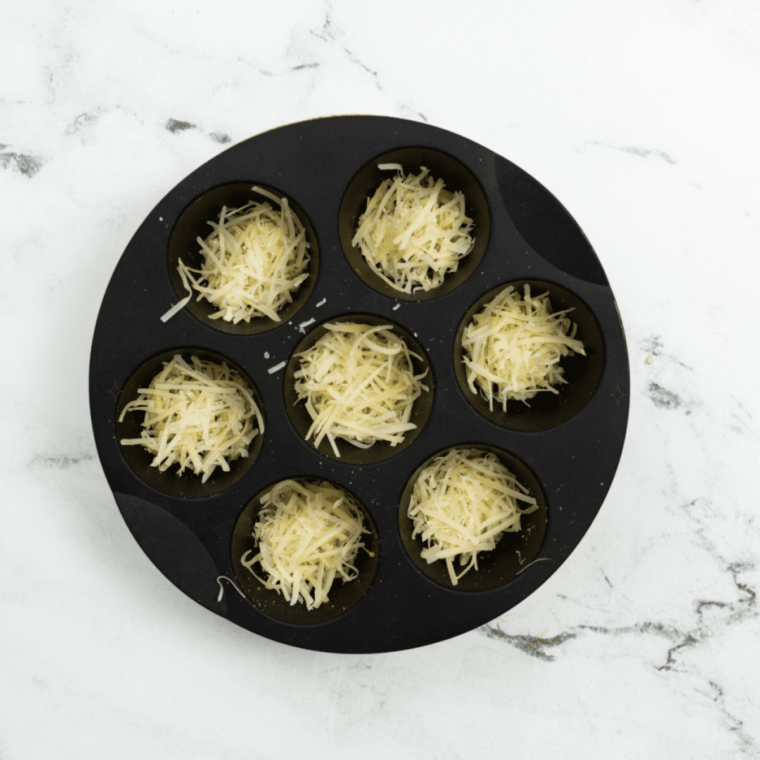 Tablespoon mounds of shredded cheddar flattened into thin circles on parchment