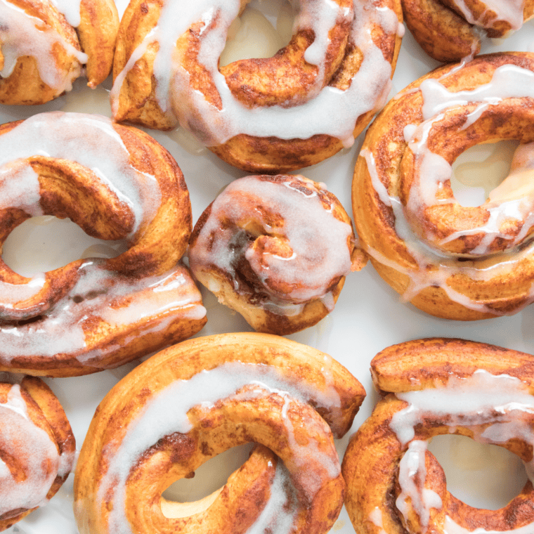 Golden brown air fryer cinnamon roll donuts drizzled with sweet glaze, stacked on a white plate