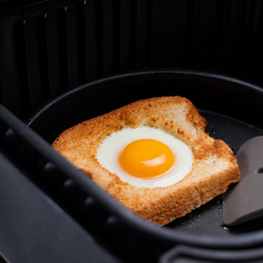 Air fryer egg in a hole on a white plate with a runny yolk running onto crispy buttered toast