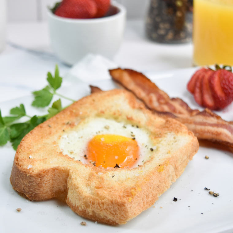Air fryer egg in a hole with a golden yolk on a white plate beside bacon and fresh strawberries