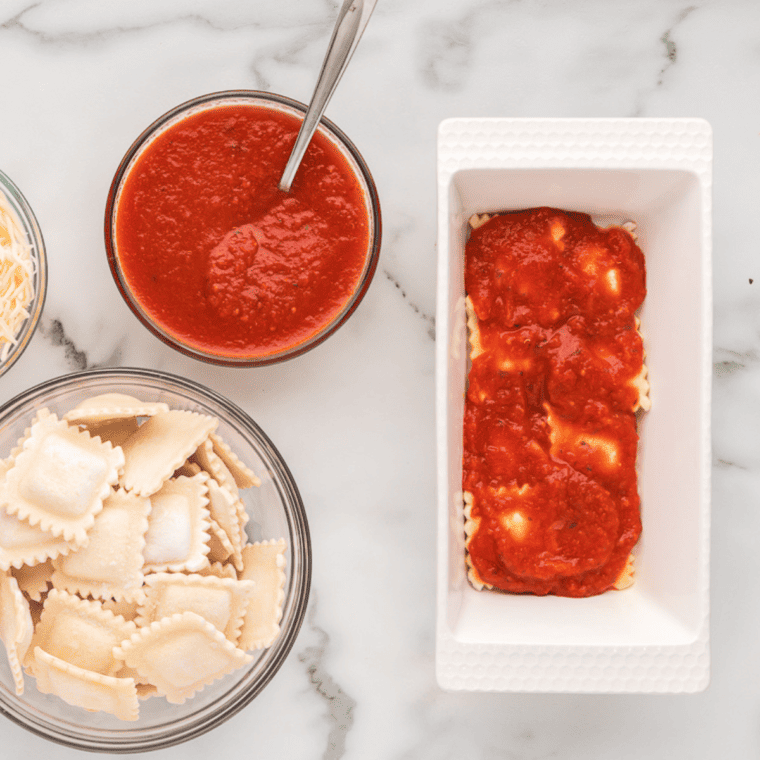 Layered ravioli with pasta sauce and cheese in an air fryer pan.
