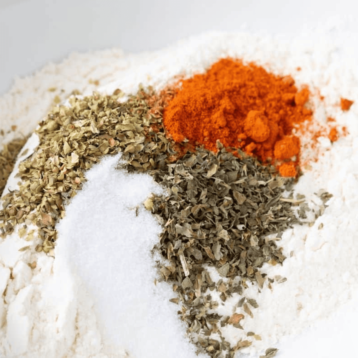 Flour and spices being combined in a small glass mixing bowl with a whisk.