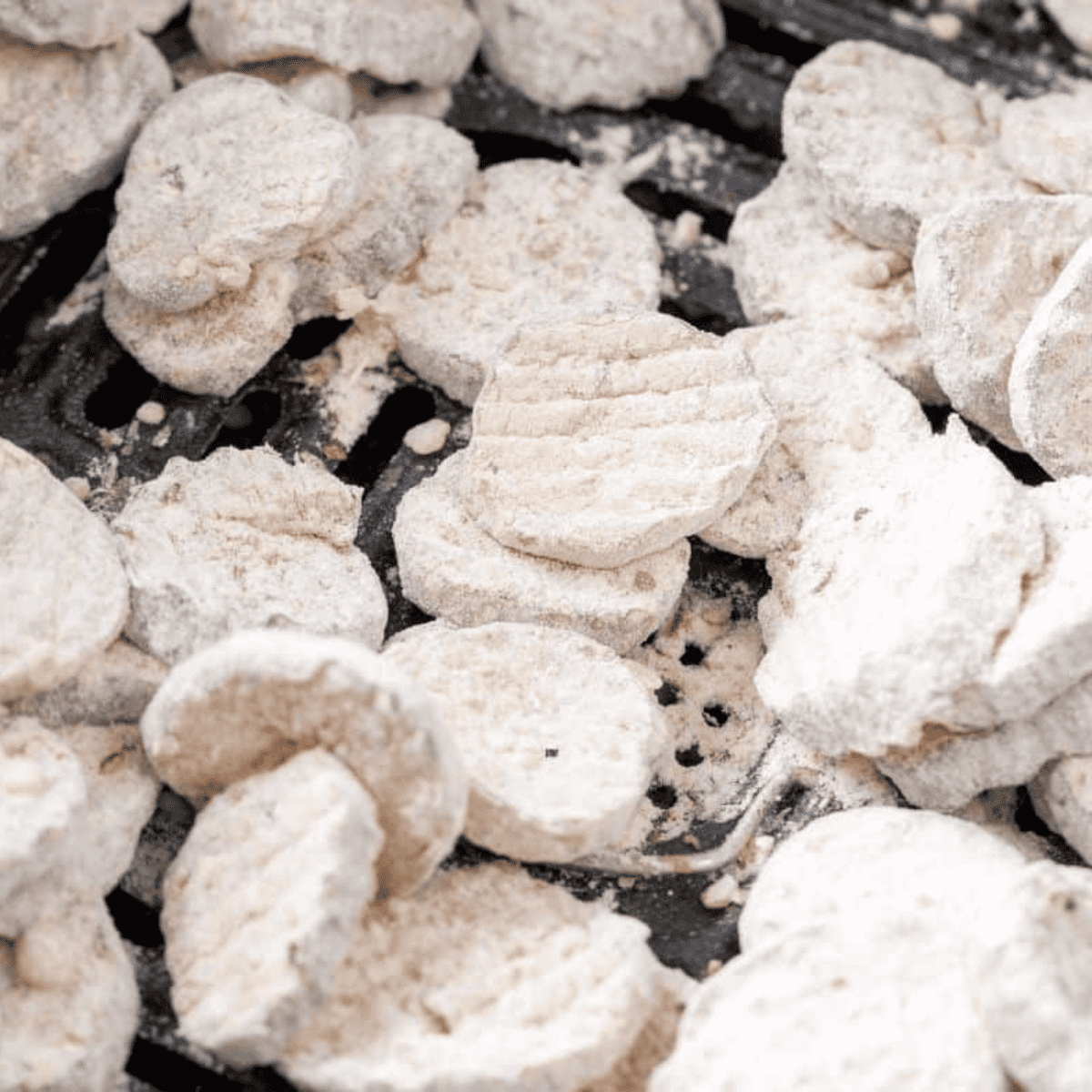 Battered pickle chips arranged on an air fryer tray sprayed with olive oil, ready to cook.