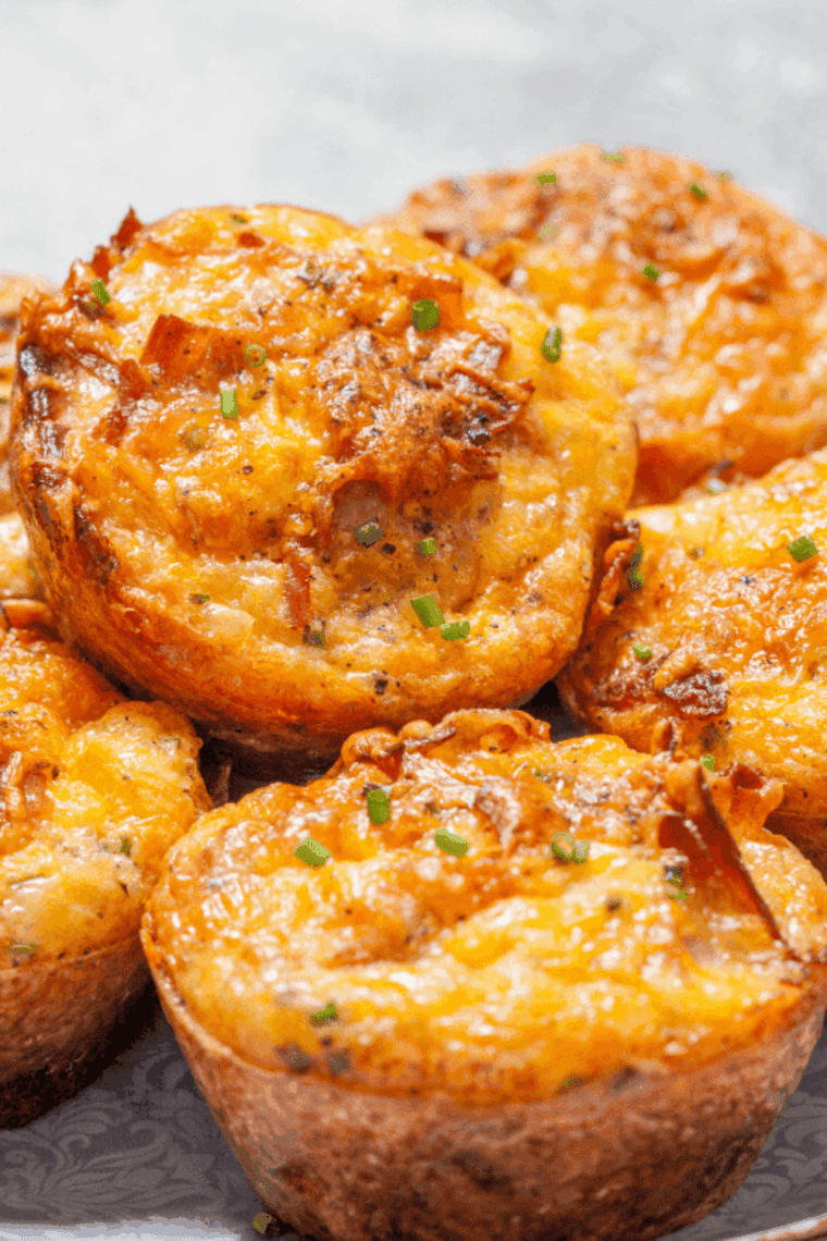Close-up of golden brown air fryer savory muffins filled with diced ham and melted cheddar cheese, served in a basket with fresh herbs.